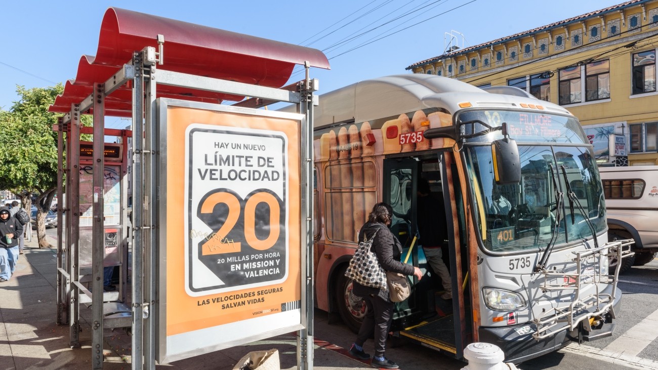 Vision Zero SF bus ad in Spanish showcasing the new reduced speed limit of 20 miles per hour. One individual is entering the bus