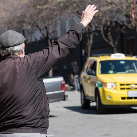 Person with hat raising arm to hail yellow tax cab 