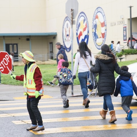 Crossing guard holding stop sign with adults and children crossing in crosswalk
