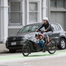 Adult with two children riding in cargo bike in a green painted bike lane