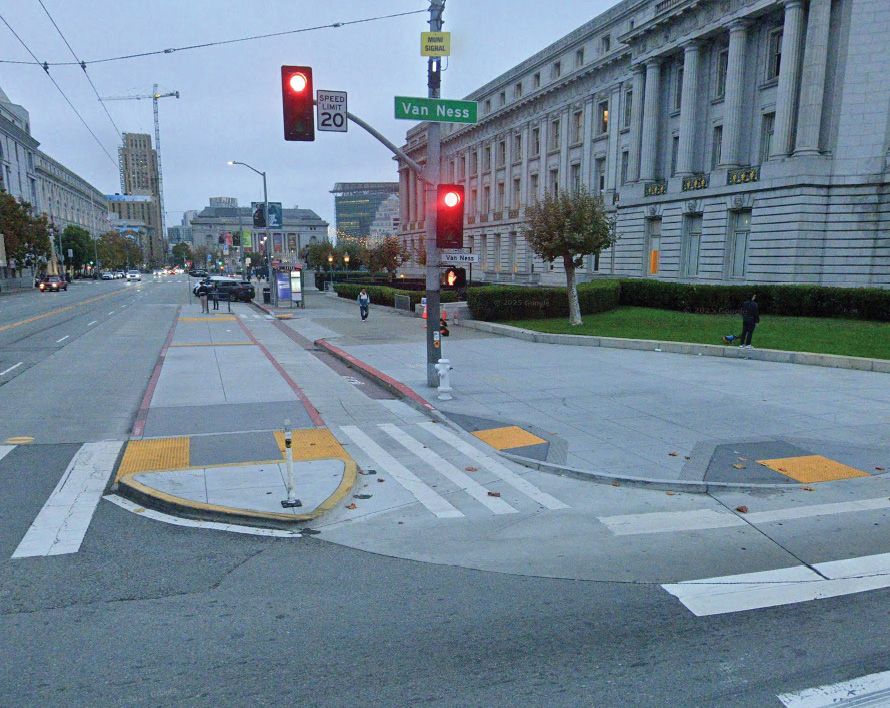 Close up of a concrete island separating a bike lane from the street. The entrance to the bike lane is rounded. There is yellow tactile paving on either side of the concrete island and leading onto the sidewalk.