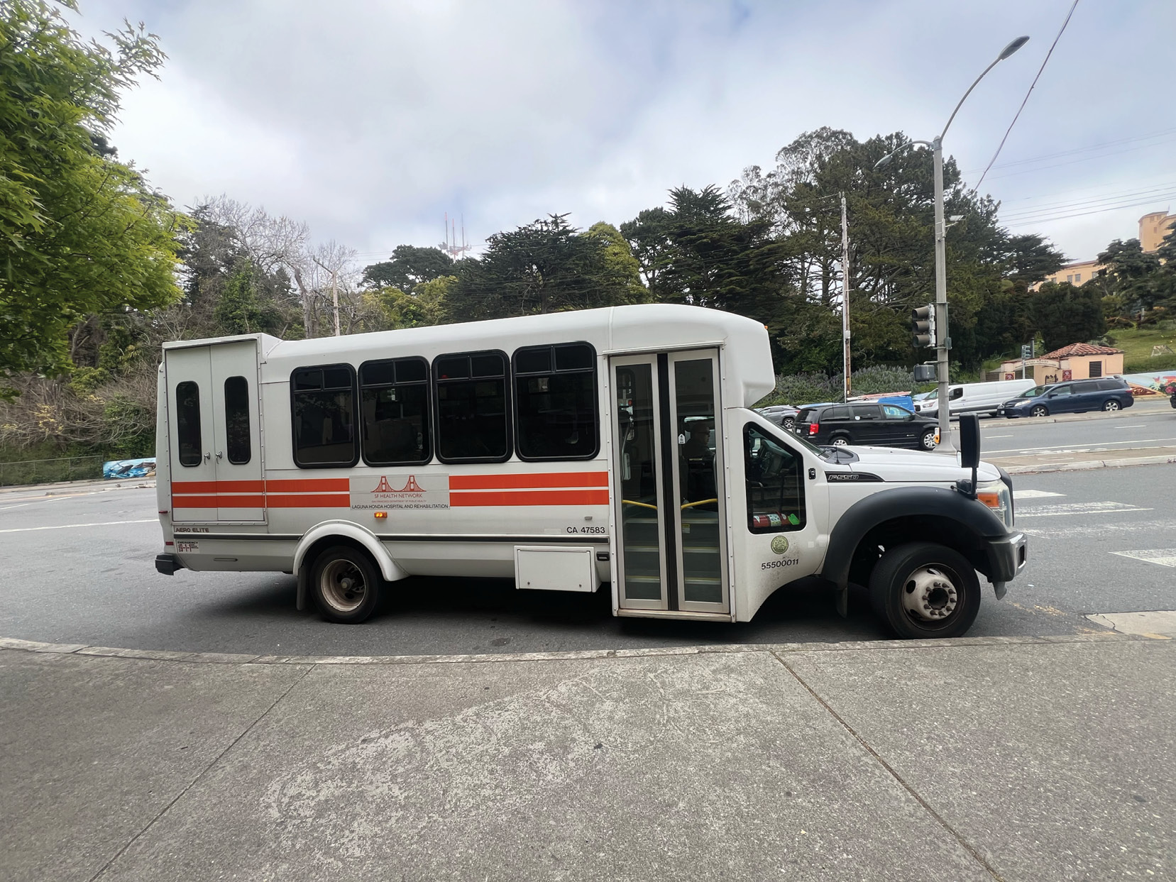 Photograph of the existing shuttle vehicle that provides service between Forest Hill Muni Station and Laguna Honda Hospital. The shuttle is shown parked along the curb and represents the mobility service currently available to hospital staff, residents, visitors, and patients.