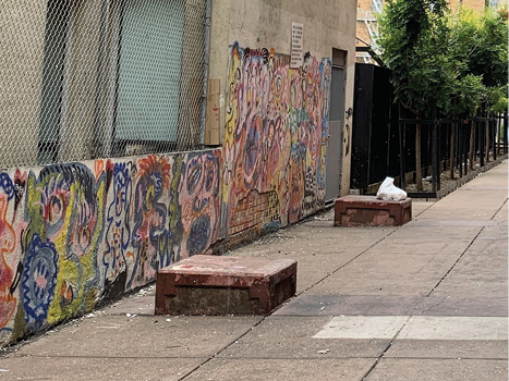 Two short, dark red concrete blocks set into the street with a row of trees in the background.