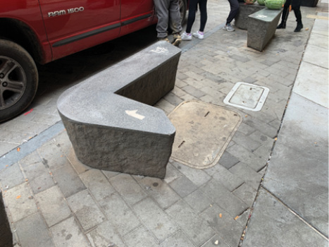 A close up of an L-shaped concrete bench on the sidewalk.