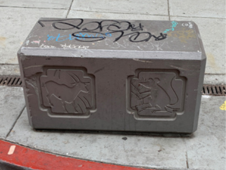 A rectangular block with carvings of an ox and a mouse on the front, mounted to the edge of the sidewalk in front of a red curb.