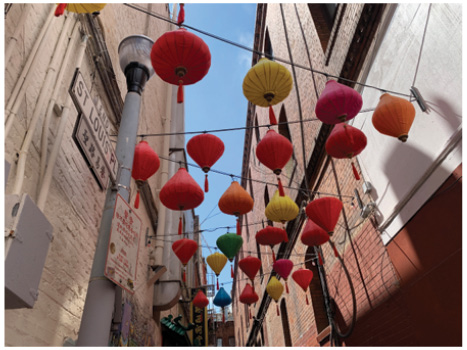 A view looking up at bulb-shaped red and yellow lanterns, strung in a criss-cross pattern across a narrow alleyway.
