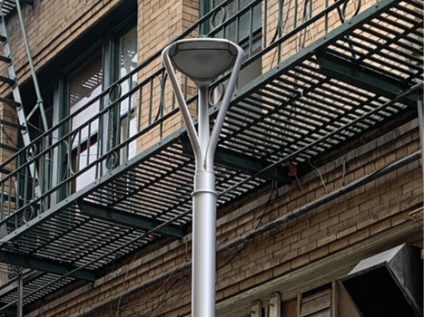 A close up of a standard street light with a building facade and fire escape in the background.