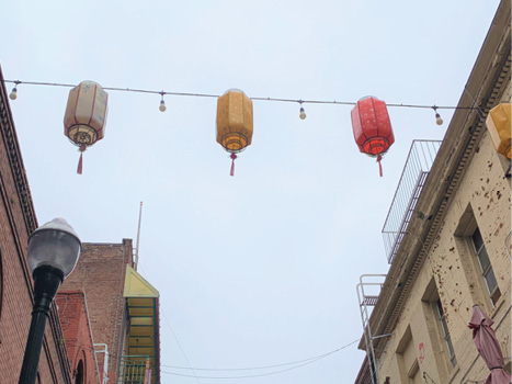 A string of three cylindrical lanterns in white, yellow, and red, against a cloudy sky.