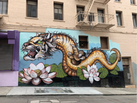 A large mural of an orange dragon with two lotus flowers against a blue and green background painted on the side of a building.