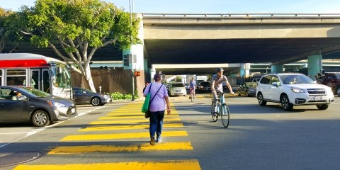 A freeway ramp intersection with cars, people walking, and people biking