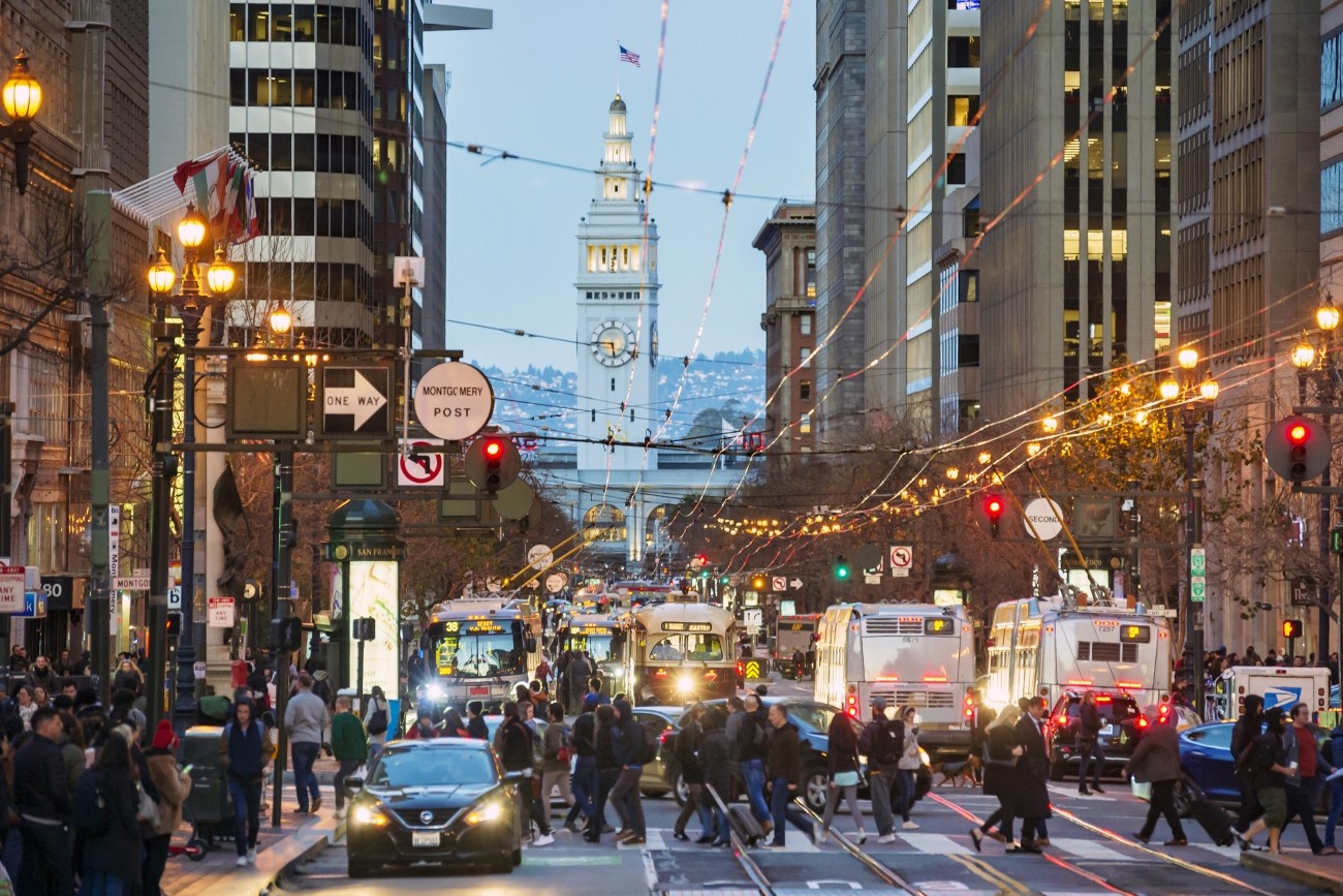 An image of buses and people walking on Market Street in the early evening