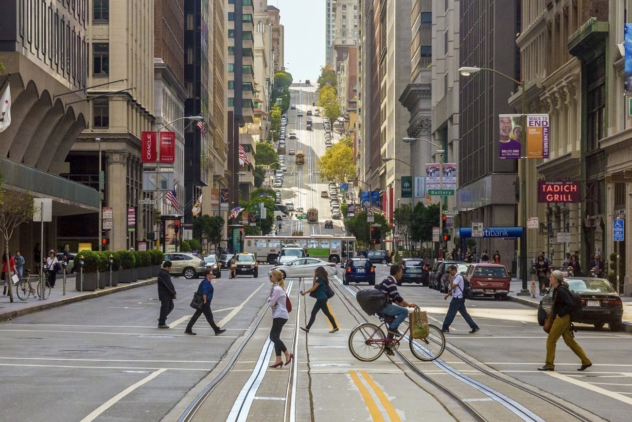 A photo of people walking and biking on Market Street, with a bus and cars in the background