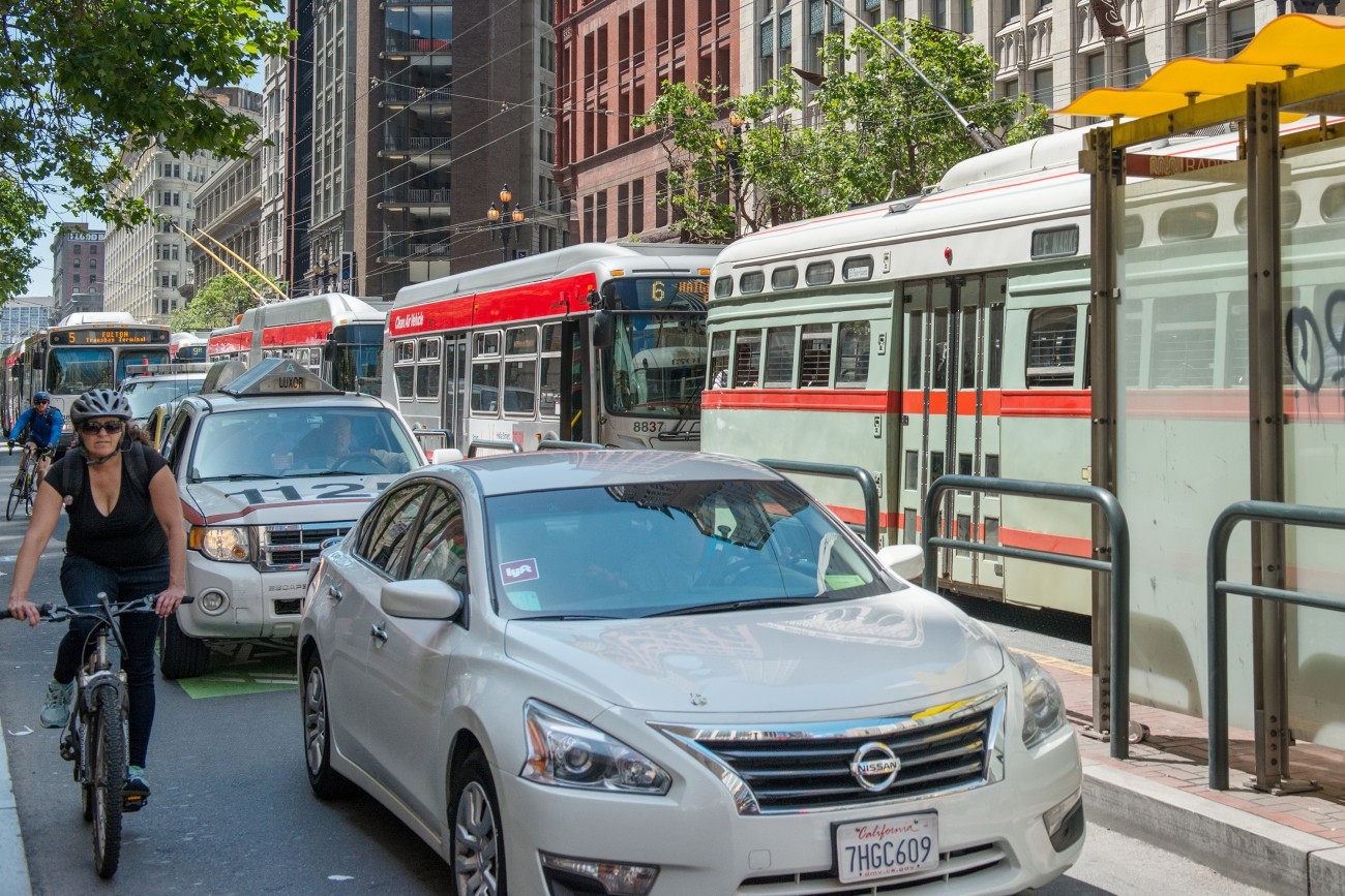 TNC vehicle on Market Street with transit and a bicyclist