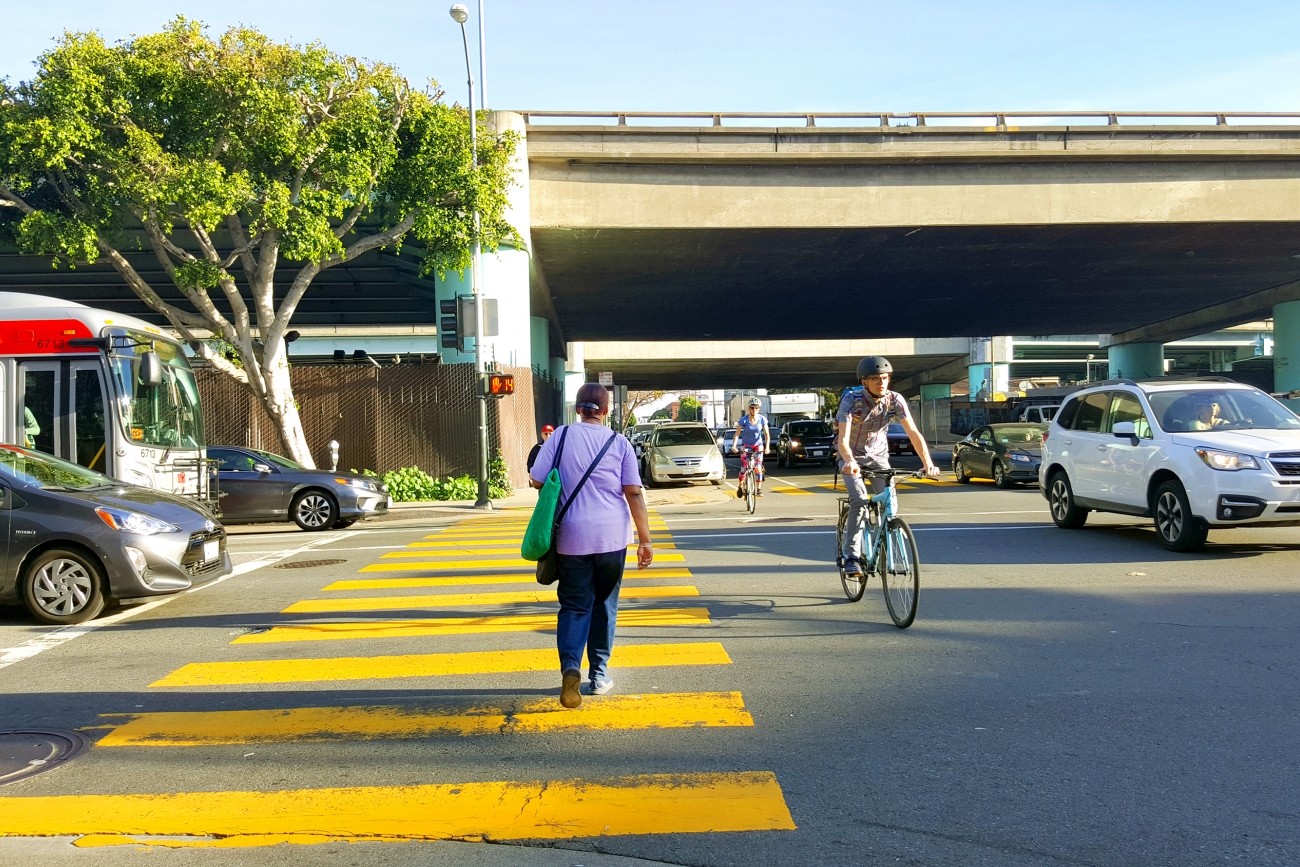 A freeway ramp intersection with cars, people walking, and people biking