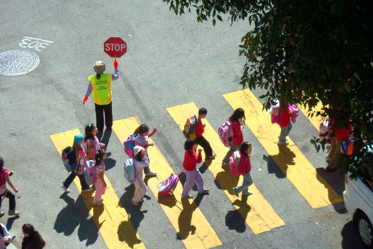 Kids crossing the street in a yellow crosswalk with a crossing guard