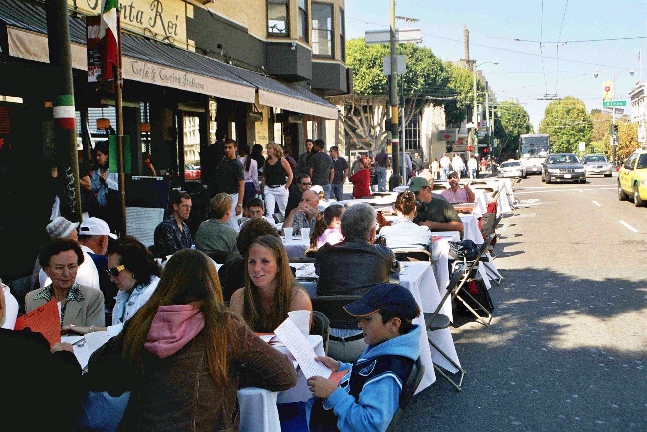 People eating on tables in parking spots in front of a cafe 