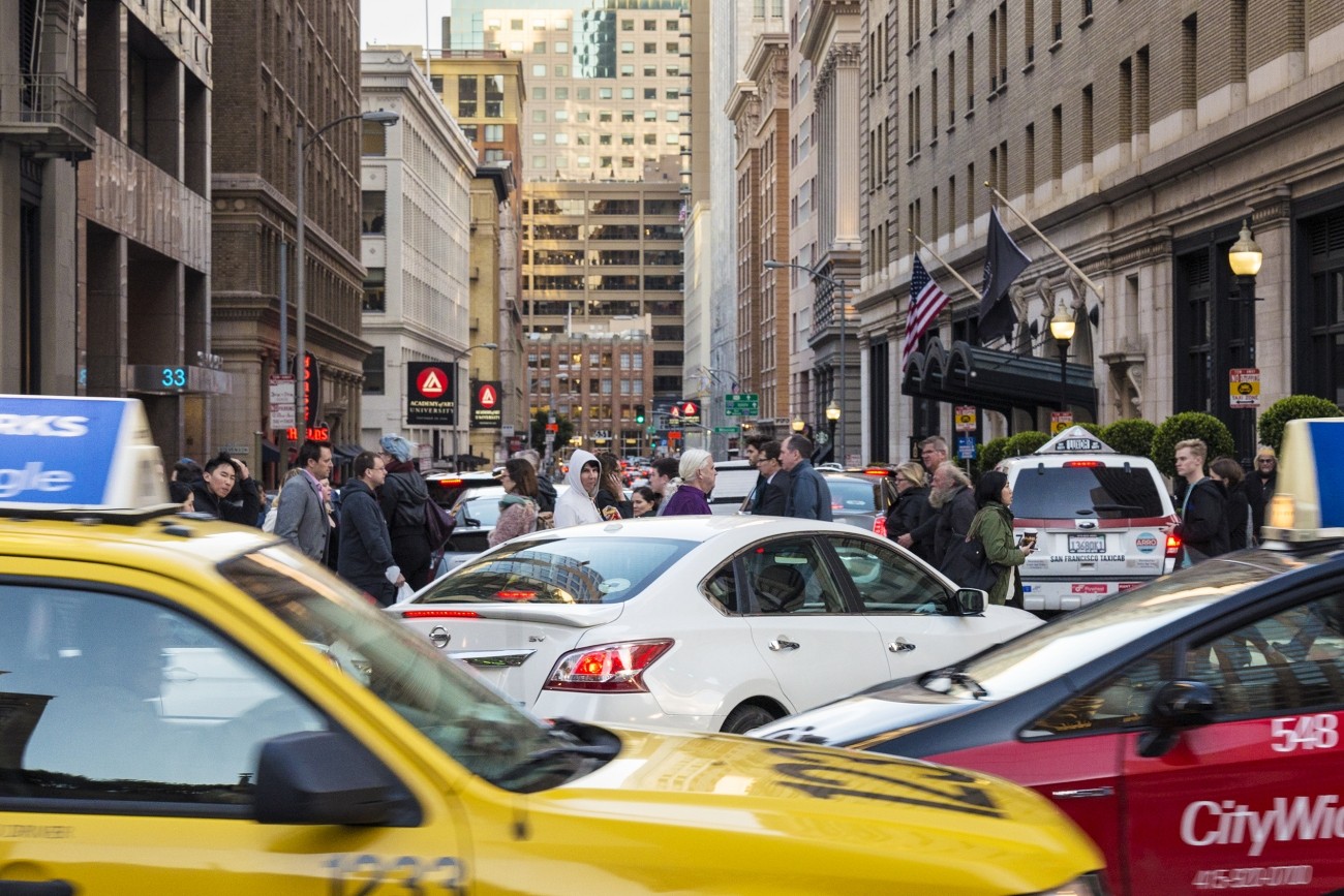 Taxis, an Uber, other cars, and people walking in congested downtown San Francisco