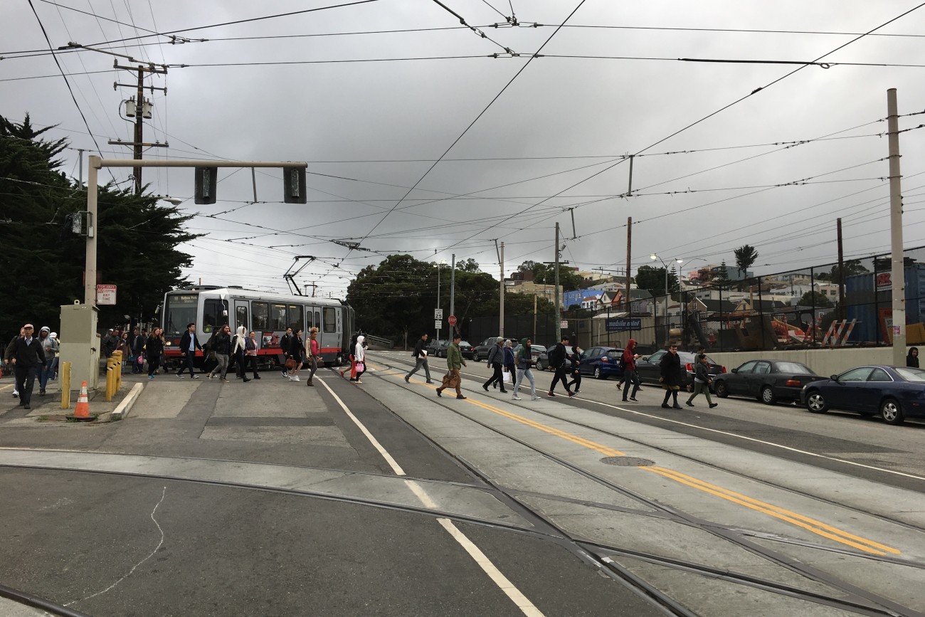 People crossing San Jose Avenue after exiting the Muni light rail. 