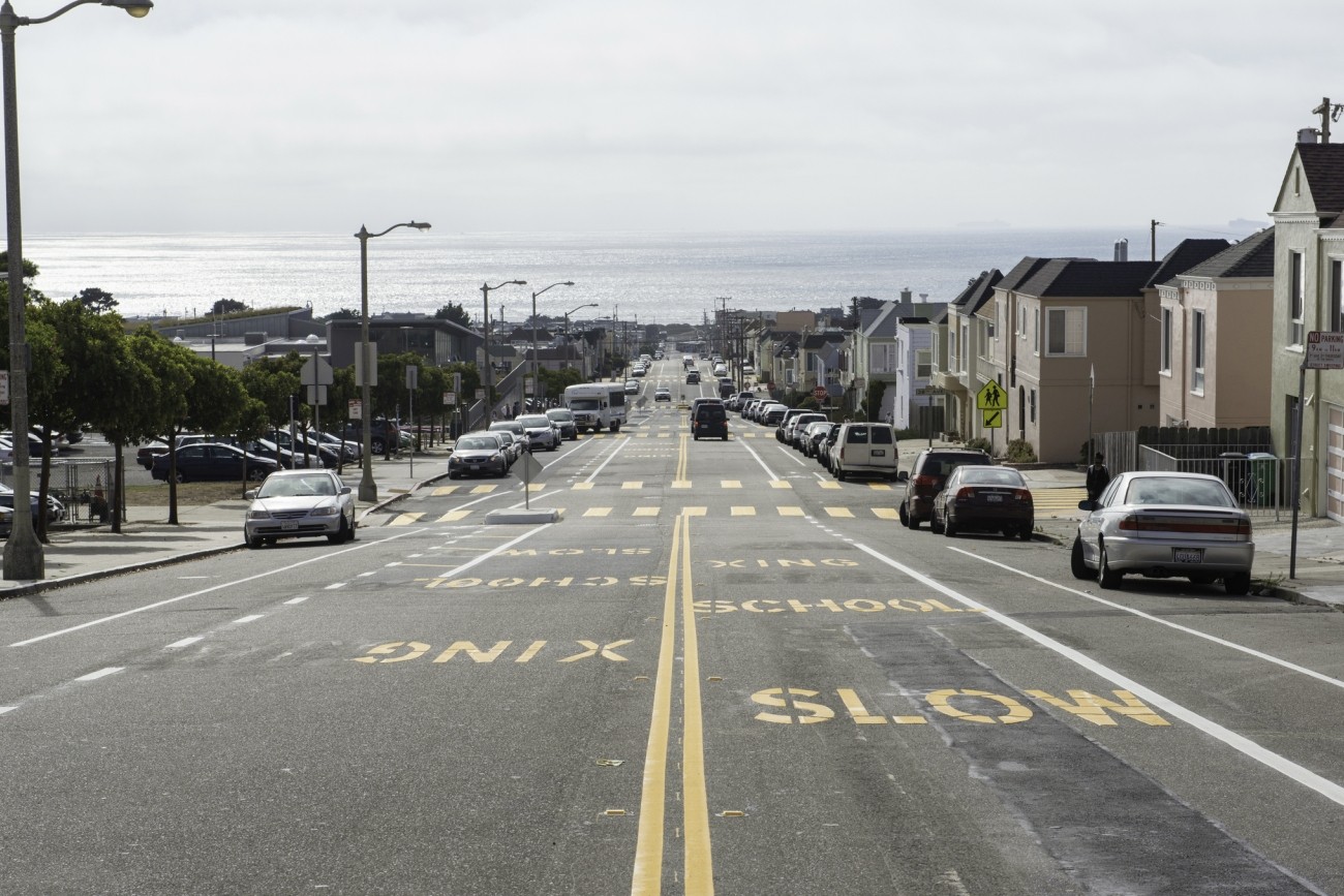 Ortega Street looking west toward the Pacific Ocean. "Slow school xing" is stenciled in yellow letters on the pavement. 