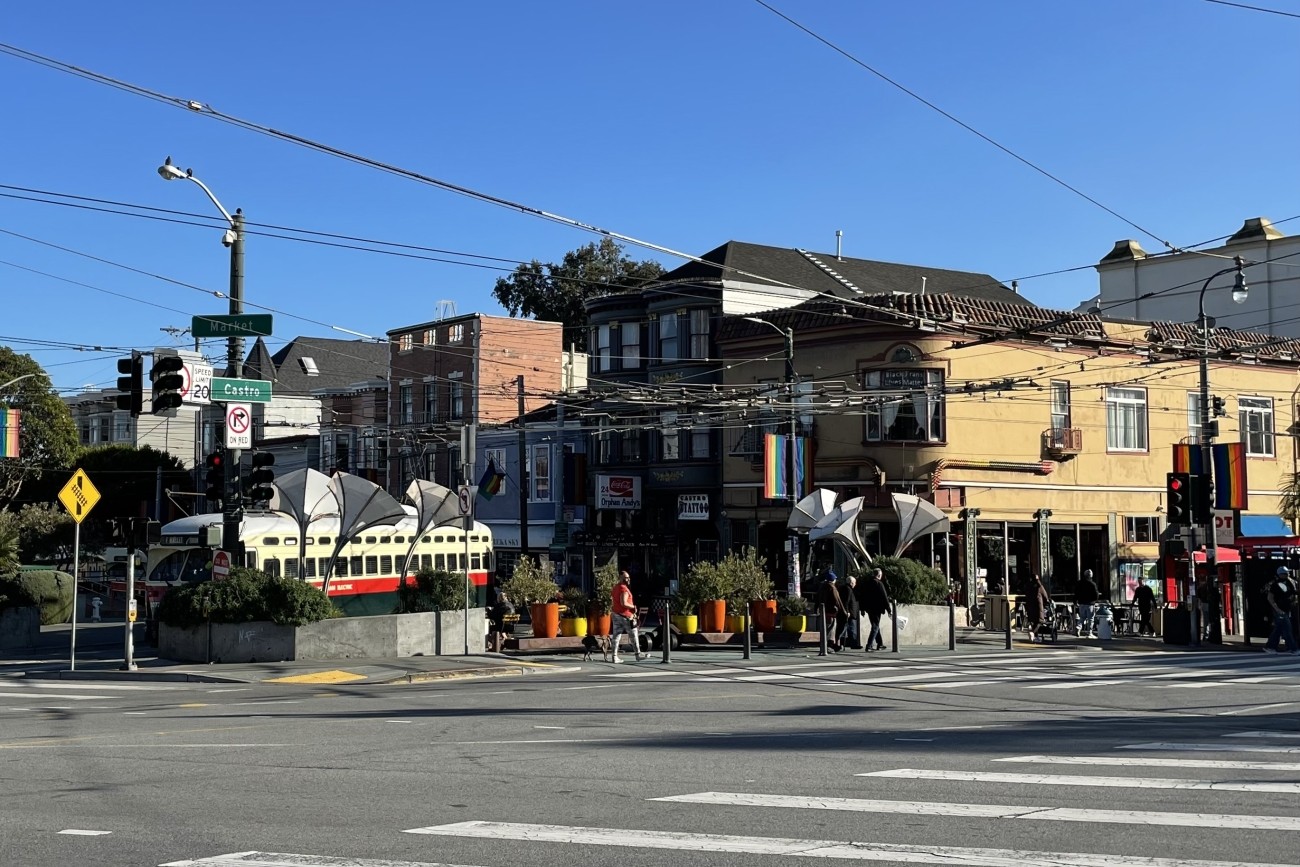 Street-level view of sunny Jane Warner Plaza and intersection of Market and Castro; a streetcar is turning from 17th onto Market Street.