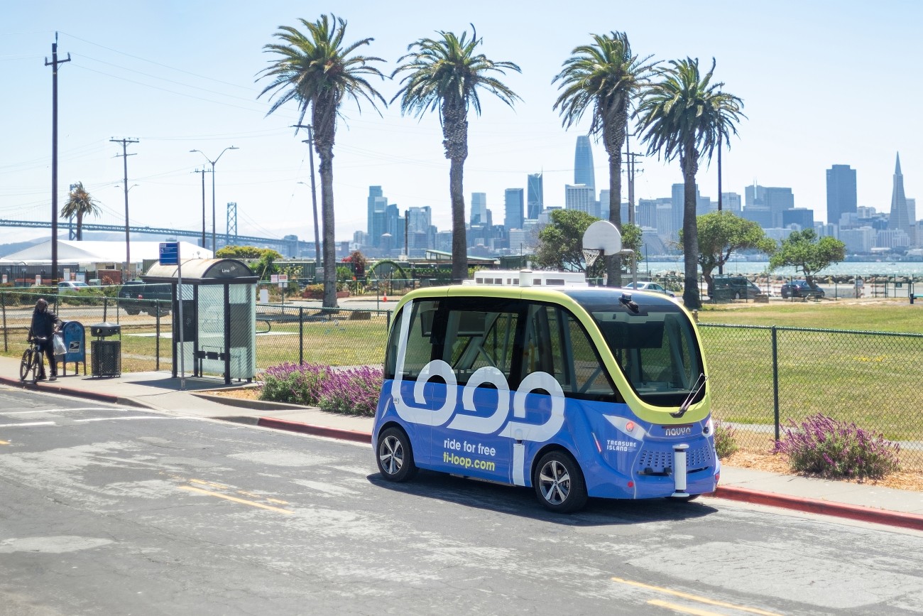 A Loop shuttle vehicle on Avenue B on Treasure Island. The San Francisco skyline is visible in the background.