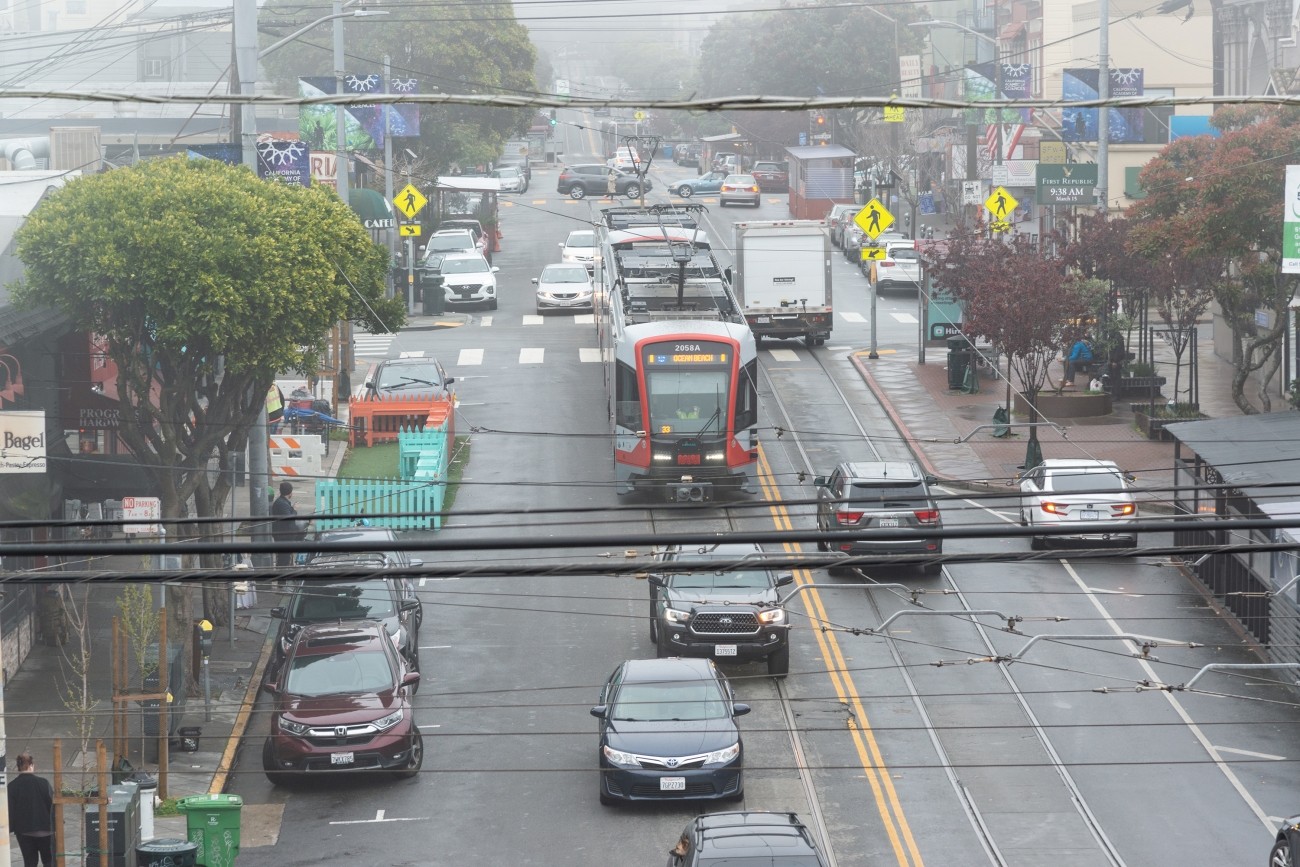 An N Judah streetcar crosses 9th Avenue at Irving in moderate traffic.