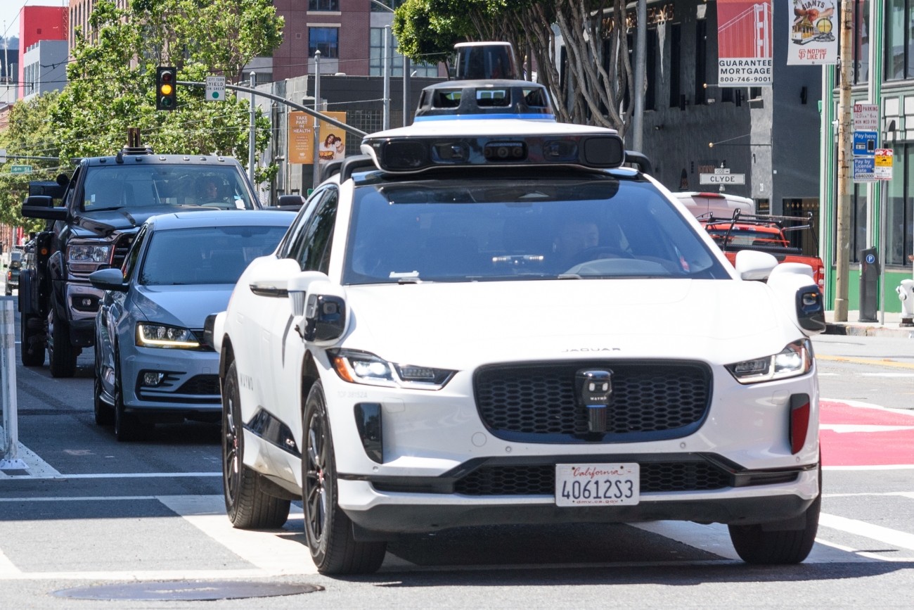 An autonomous vehicle drives through an intersection in SoMa, followed by two human-driven vehicles.