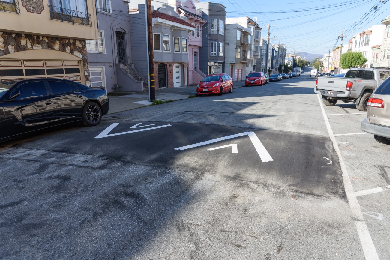 Speed hump with arrows and cars parked against the curb. 