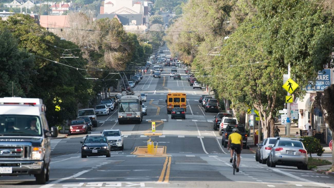 An image taken at Fulton and Arguello, looking down Arguello, with a car and a person biking