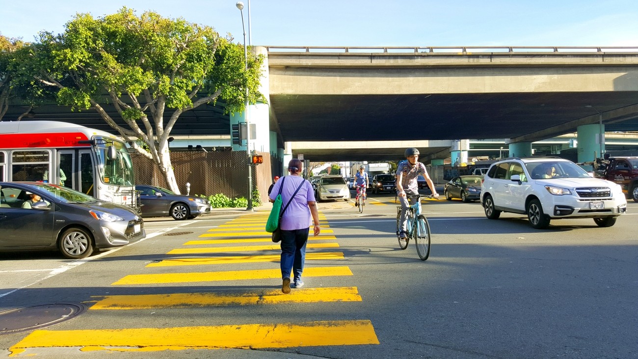A freeway ramp intersection with cars, people walking, and people biking
