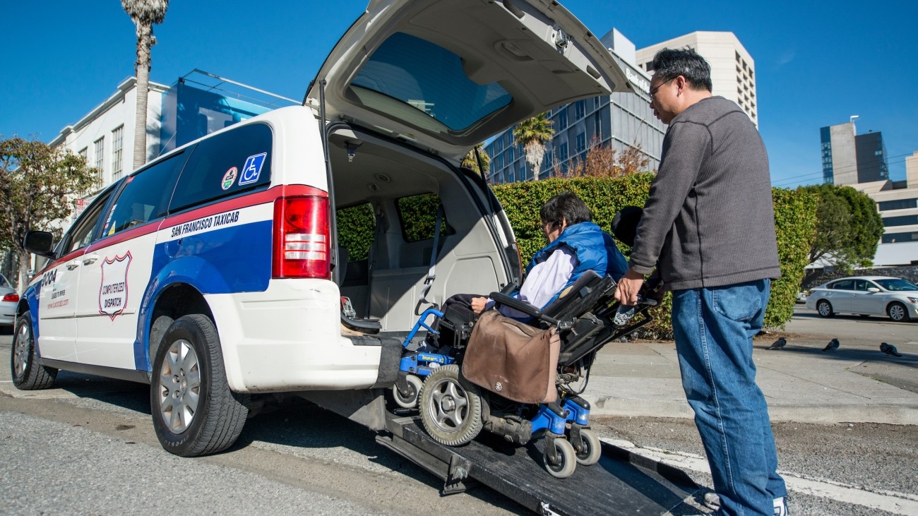 A taxi driver helping someone with a wheelchair get into a taxi