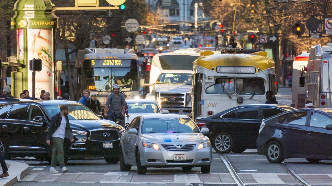 An Uber/Lyft vehicle among bicyclists, other cars, buses, and streetcars on Market Street
