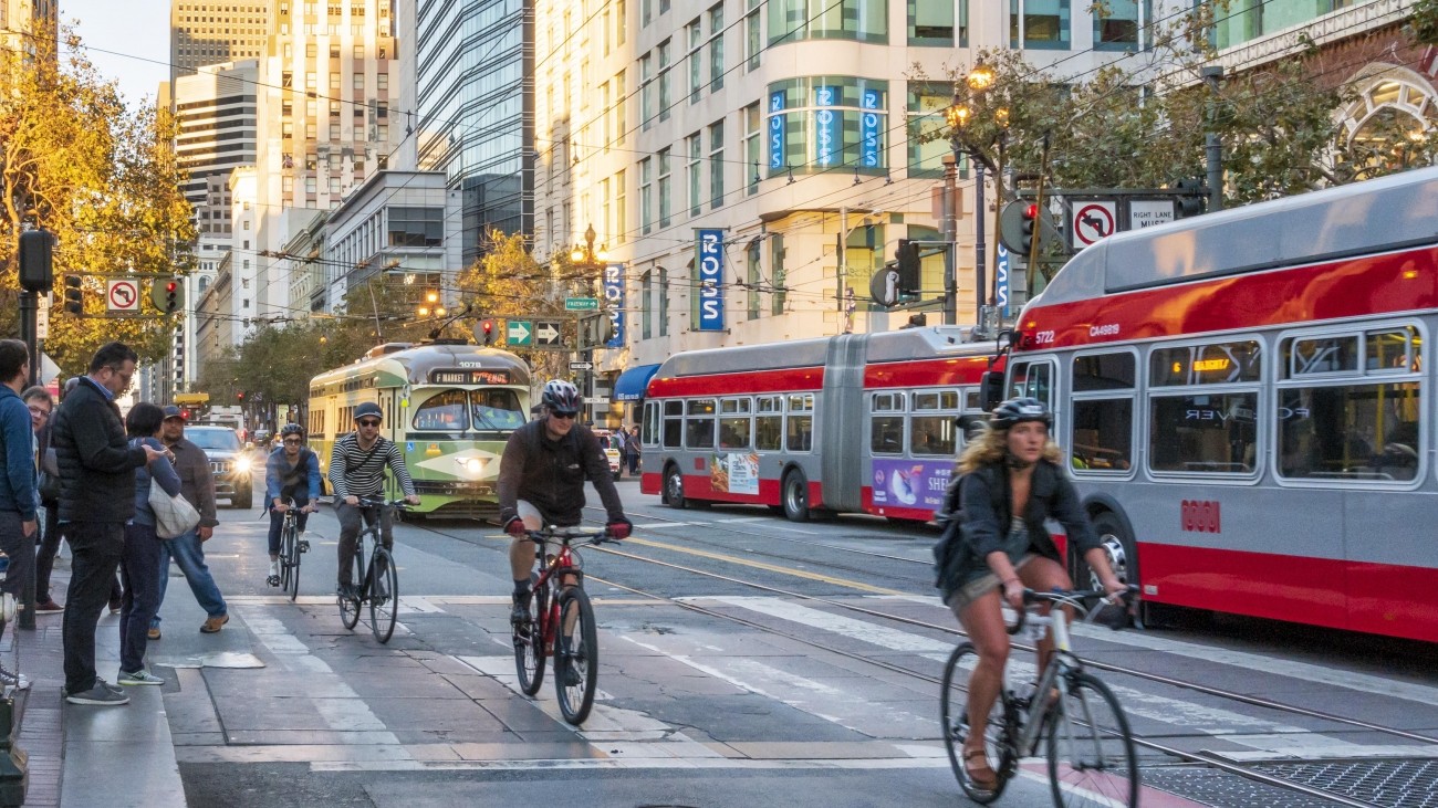 People biking with a bus and streetcar in the background