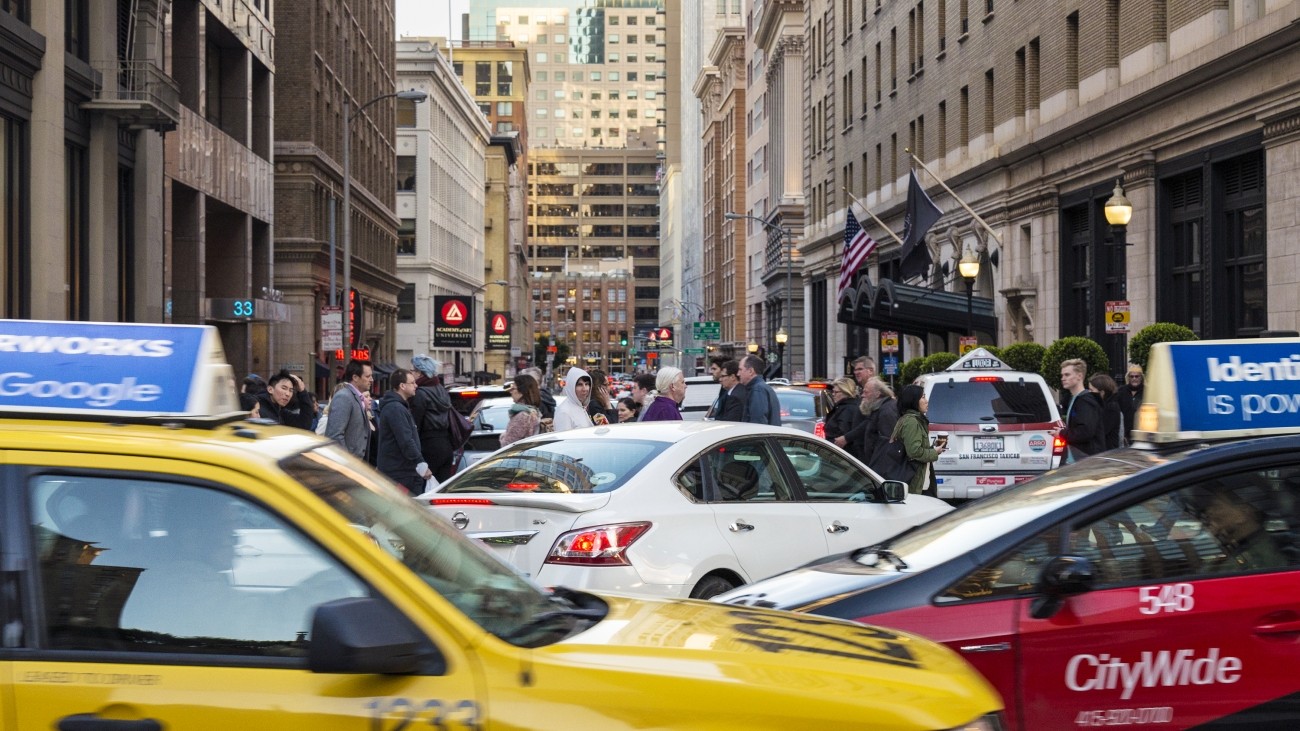 Taxis, an Uber, other cars, and people walking in congested downtown San Francisco
