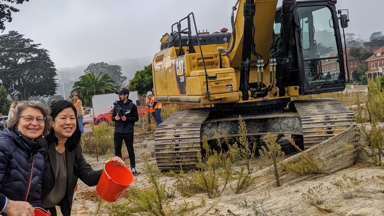 A picture of Tillly Chang and  Helena "Lenka" Culik-Caro holding buckets of dirt at the groundmaking site