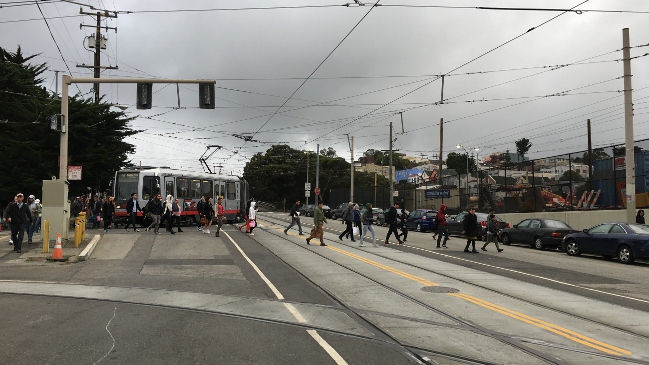 People crossing San Jose Avenue after exiting the Muni light rail. 