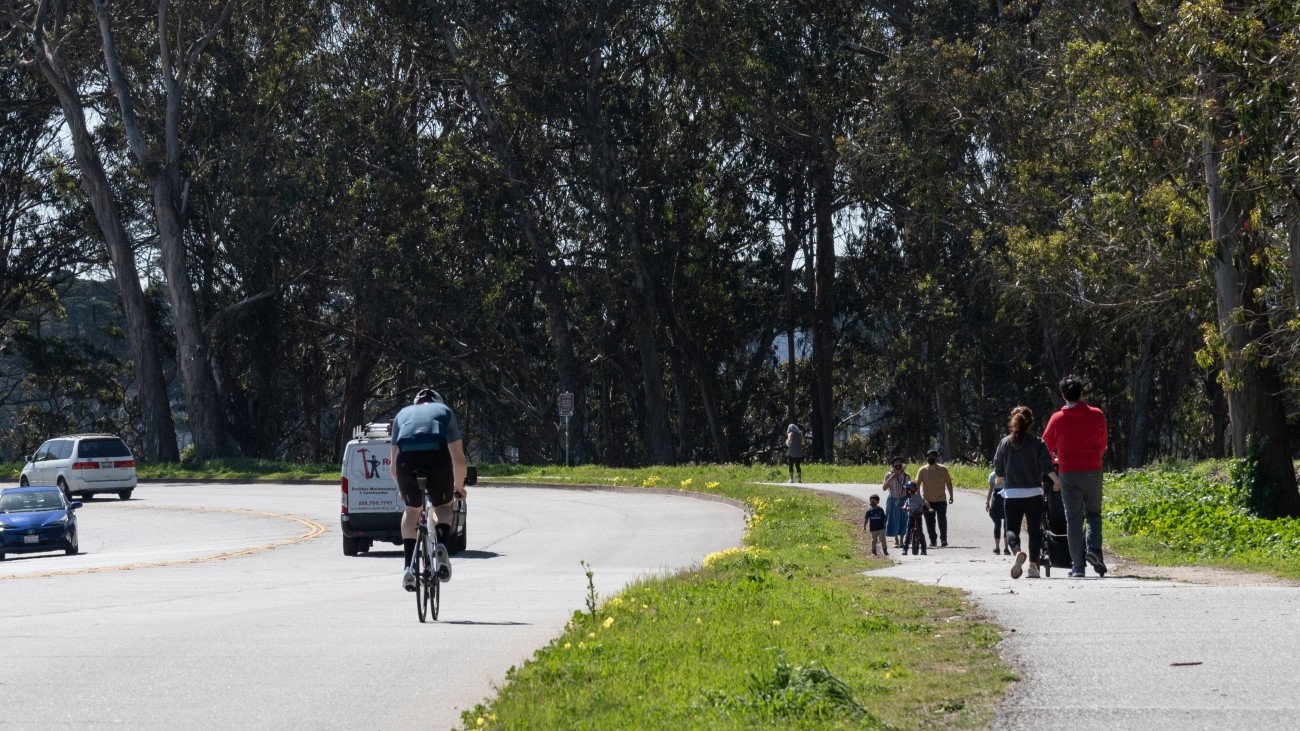 Pedestrians on path and bike and vehicles on road along Lake Merced