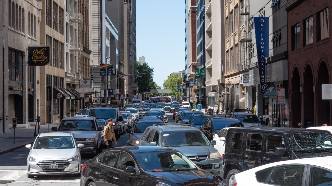 Many cars on a road with buildings in the background.