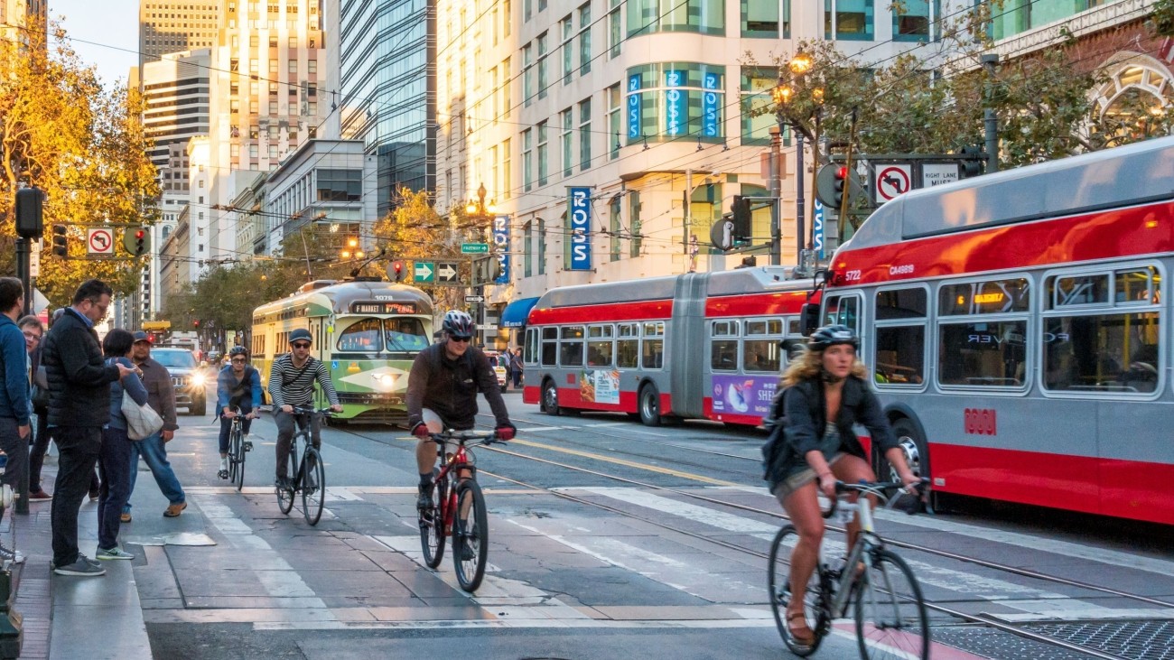 Bikers, buses, and cars traveling on a street in downtown San Francisco.