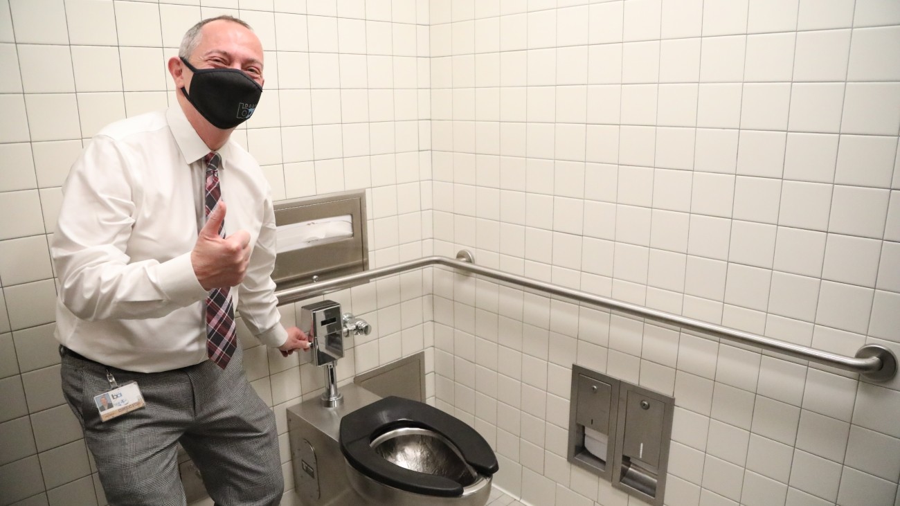 BART official flushes the toilet as he stands next to it while giving a thumbs up.