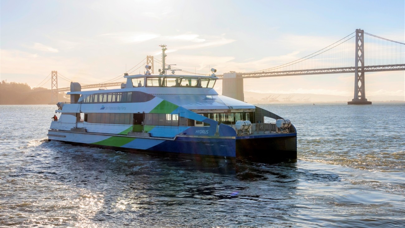 A ferry travels across the San Francisco Bay on a sunny day with the Golden Gate Bridge in the background.