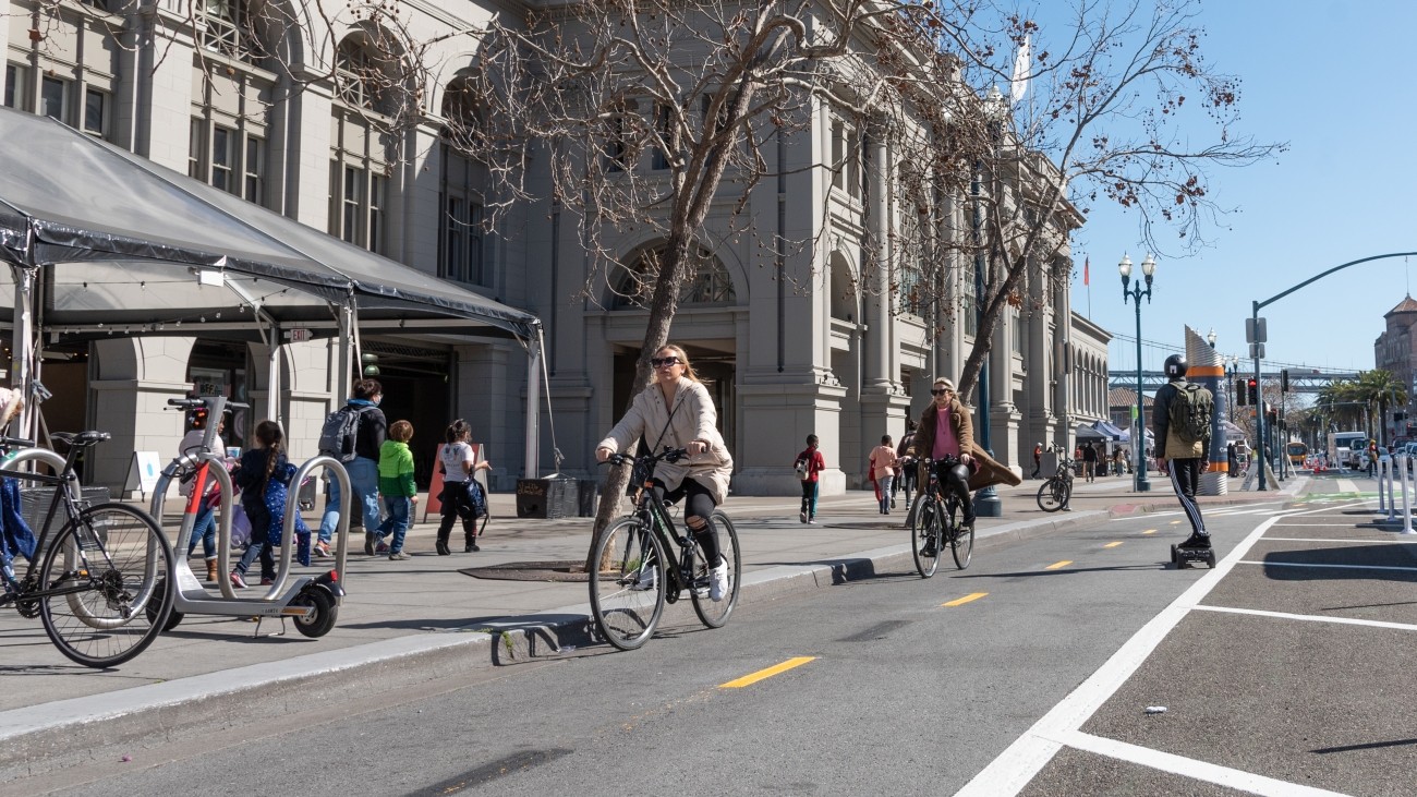 People riding on bikes and skateboard along Embarcadero by Ferry Building