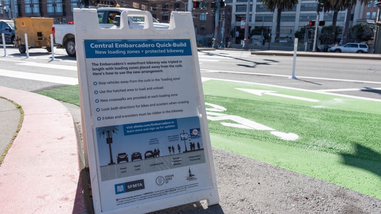 Standing sign featuring info about Central Embarcadero Quick-Build and a graphic on the road