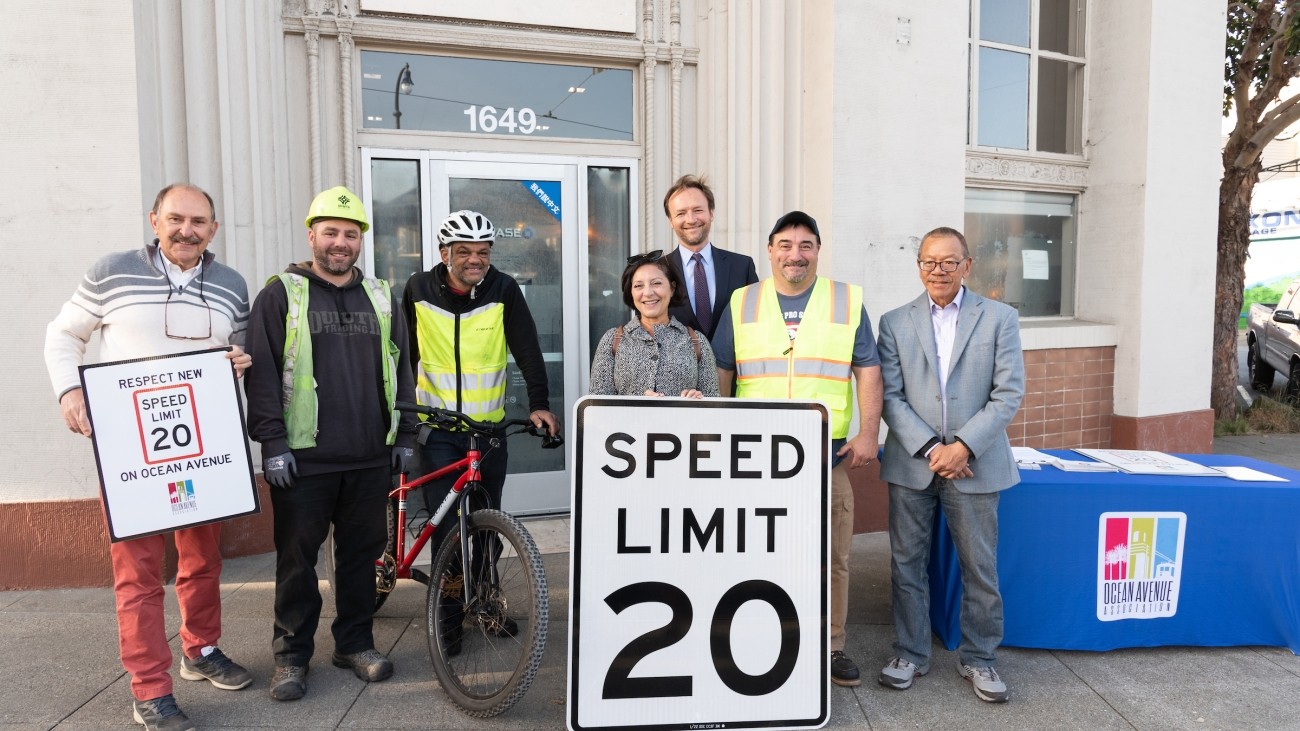 Transportation officials, community advocates, and city staff posing with 20 mph speed limit sign