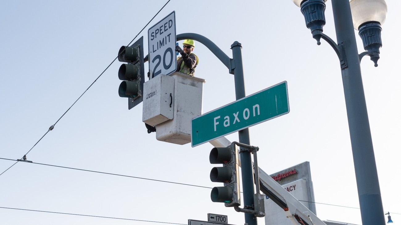Worker installing a 20 mph sign on traffic post at Faxon and Ocean
