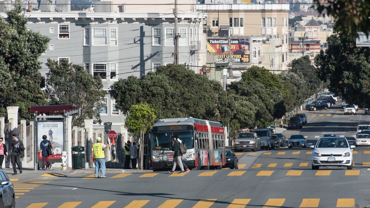 Cars and Muni bus on the road, crossing guard and youth in crosswalk