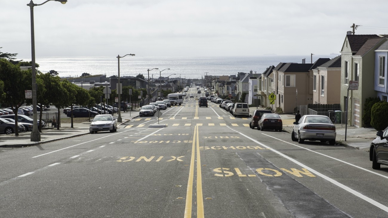 Ortega Street looking west toward the Pacific Ocean. "Slow school xing" is stenciled in yellow letters on the pavement. 