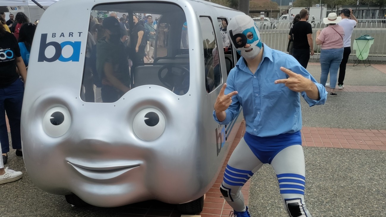 BART mascot posing next to mini BART train. 
