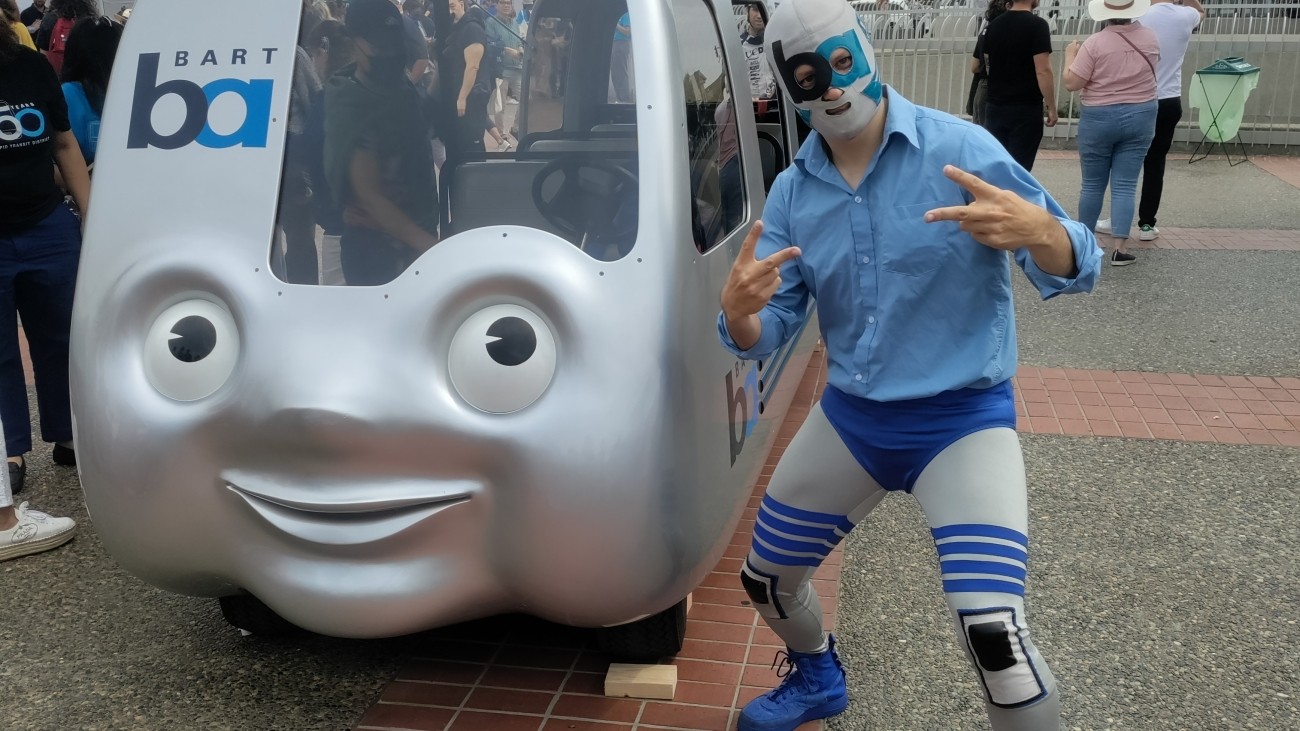 BART mascot posing next to mini BART train. 