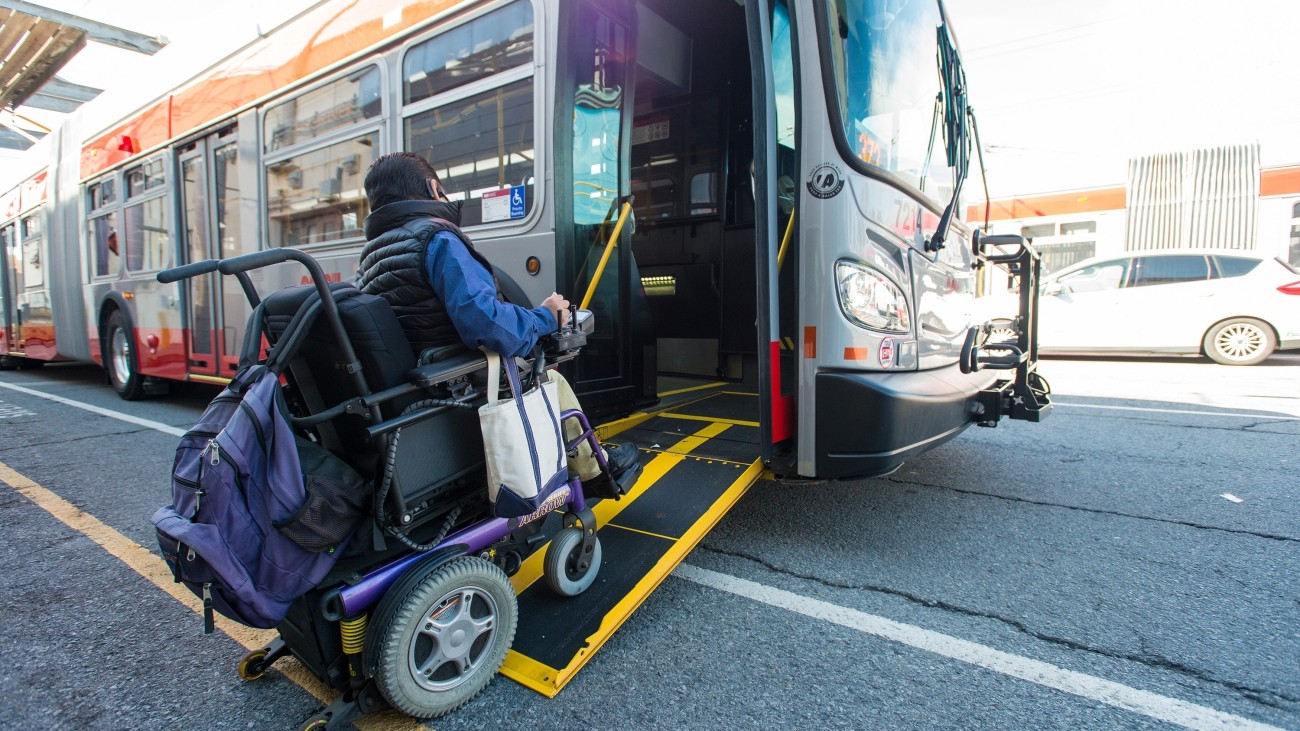 A person in a wheelchair boards a Muni bus using a retractable ramp